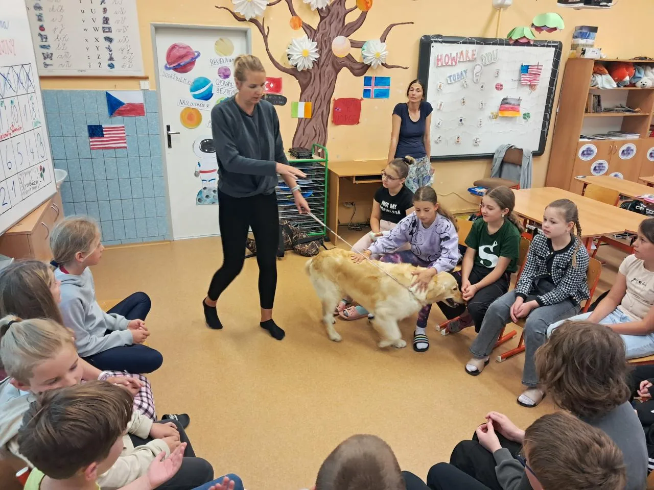 Lucie vede Alminku před třídou dětí na návštěvě ve škole